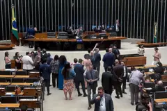 Deputado Glauber Braga sentado na mesa diretora. Parlamentares estão ao redor