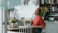 Młoda kobieta siedzi przy stoliku w kawiarni z laptopem i pałeczkami do gry w perkusję