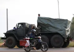 A man drives past a military vehicle heading towards the border, amid deadly clashes between Thailand and Cambodia along a disputed border area, in Srei Snam, Siem Reap Province, Cambodia, December 10, 2025. REUTERS/Kim Hong-Ji