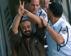 2003 archive picture of a young Marwan Barghouti, the leader of the Fatah movement, handcuffed and flashing the V-sign, in the West Bank, flanked by Israeli policemen as he is led to a police vehicle on 29 September 2003 on his way back to jail