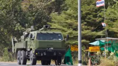 Zielona haubica stoi zaparkowana na drodze. Na maszcie w pobliżu powiewa flaga Tajlandii.