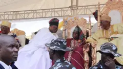 Gomina Ibikunle Amosun wọ agbada ati sokoto funfun ati fila asọ ti wọn mu fun ọdun Owu ti ọdun yii, o kọju si Oloye Olusegun Obasanjo, lati baa sọrọ, Obasanjo wọ agbada ati sokoto asọ oke Alaari, to si de fila asọ oke kan naa pẹlu Amosun, ti Olowu tilu Owu naa si joko ni ẹgbẹ wọn, ẹni to wọ asọ oke Sanyan, to si de ade sori. Awọn osisẹ ọlọpaa to n sọ wọn wa niwaju wọn.
