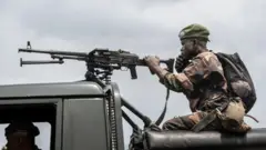 Un soldat des Forces armées de la République démocratique du Congo (FARDC) tient une mitrailleuse montée sur un support et parle au téléphone le long de la route menant à l'entrée de la ville de Sake, en janvier 2025.