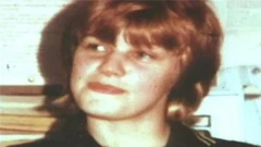 Archive photograph of Karen Price. She has mousy brown hair but into a full fringe and shoulder length mullet. The image is grainy but she has blue eyes, red lips and looks away from the camera.