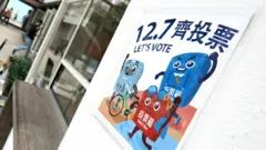 香港炮台山「油街實現」藝術空間內一張貼在牆壁上的「12.7齊投票」大尺碼宣傳貼紙(BBC中文圖片4/12/2025)