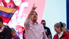 委內瑞拉總統尼古拉斯·馬杜羅身穿有領襯衫,袖子捲起,內搭白色T恤,站在巨型螢幕前,指向天空