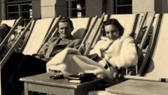 Una pareja en unas tumbonas miran sonrientes a la cámara en una imagen en blanco y negro.