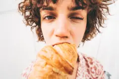 Obinrin alawọ funfun to n jẹ croissant to si n ṣẹ oju kan