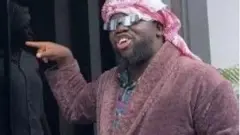 Mama Deola asọ obinrin, we gele, to si n kan ilẹkun kan.