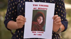 تصویر زنی که عکس چاپ شده از پرتره معروف شربت گل را به دست گرفته. چهره زن نمایان نیستن تنها دستهایش در تصویر دیده میشود. در پلاکاردی که زن در دست دارد به انگلیسی «ارزش من زیبایی من» نوشته شده است.