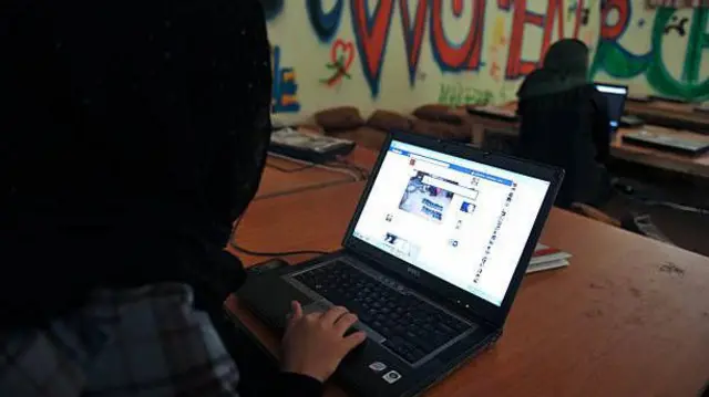 تصویر یک زن در پیش روی کمپیوترش. او پشتش به سمت دوربین است و در لپ تاپش شبکه اجتماعی فیسبوک را باز کرده است.