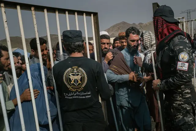 ځينې افغان کډوال د راجستر کېدو لپاره د تورخم دروازې ته څېرمه له پنجرې سره ولاړ دي او د طالبانو حکومت ساتونکي یې په نوبت نوبت پرېږدي.