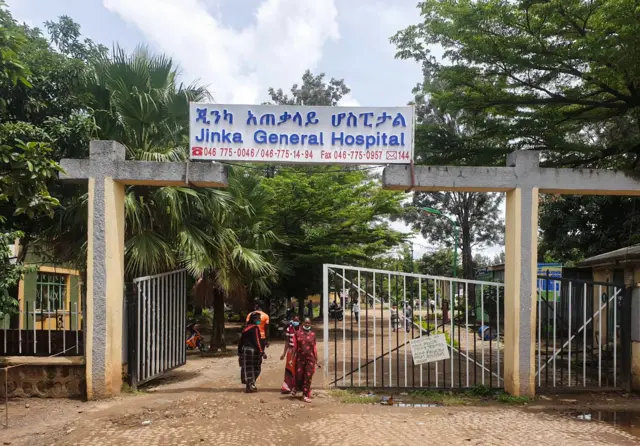 የጂንካ አጠቃላይ ሆስፒታል የሚል ትልቅ ቢልቦርድ ከተሰቀለበት መግቢያ በታች ሶስት ቀሚስ የለበሱ ሴቶች እየተራመዱ ሲወጡ ይታያል