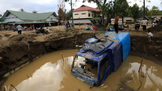 مردی در روستایی در اندونزیا، بالای لاشهی یک لاری آبی رنگ که در گل و لای و آب سیل مدفون شده است، ایستاده است.