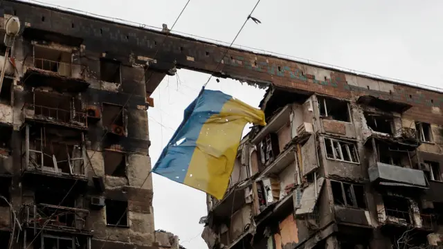 پرچم پارهشده اوکراین میان دو ساختمان بمبارانشده آویزان است.