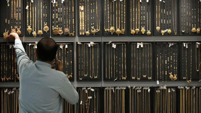 一名男子手持电话,背后展示着大量的金器。