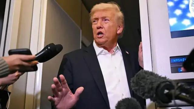 دونالد ترامپ در هواپیمای «ایر فورس وان» کنار در ایستاده و با خبرنگاران صحبت میکند. چندین میکروفون به سمت او نشانه رفتهاند. او یک کت آبی تیره و پیراهن سفید بدون کراوات پوشیده است. دست راست ترامپ بالا رفته و دهانش هنگام صحبت باز است