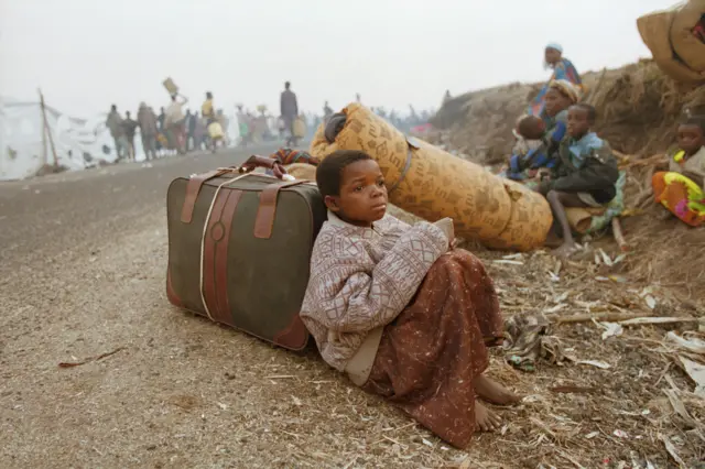 A Rwandan girl sitting on a roadside with some luggage