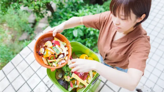 ایک عورت بچے ہوئے کھانے کو کمپوزٹر میں ڈال رہی ہے