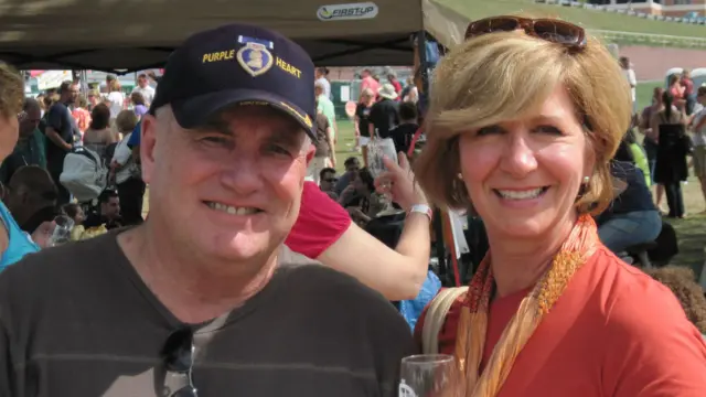 卡罗尔先生戴着蓝色帽子,韦伯女士头上架着太阳眼镜、手里拿着杯子,在户外活动中面带笑容。