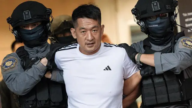 一名身穿白色阿迪达斯T 恤的男子,被两名头戴黑色头盔、穿着防护背心的警卫押送