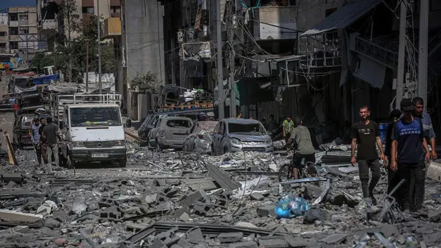 በፍንዳታ የተጎዳ ሕንጻ እና መኪኖች የሚታዩበት በፍርስራሽ የተሸፈነው የጋዛ ከተማ ሪማል አካባቢ መንገድ