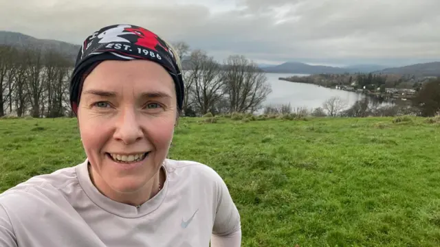 一名头戴有图案头巾的女性在草地与湖泊前自拍