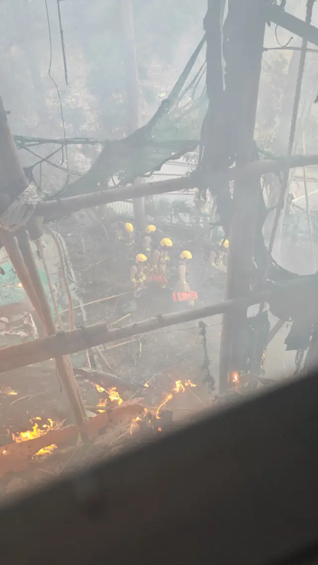 李先生从窗外望出火灾现场,前方有竹棚和被烧掉的棚网,地面是一群消防员。