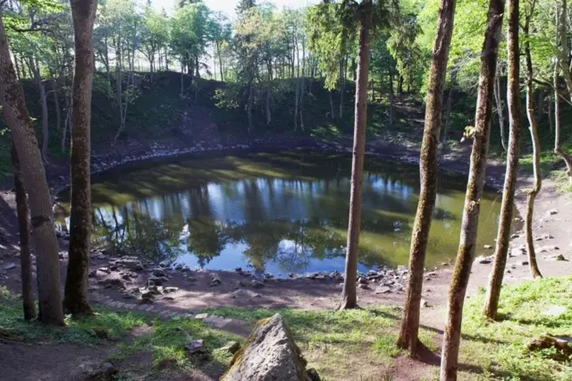 حفرة نتجت عن سقوط نيزك على الأرض منذ 4000 عام، مليئة بالمياه ومحاطة بالأشجار والعشب والطين والصخور.