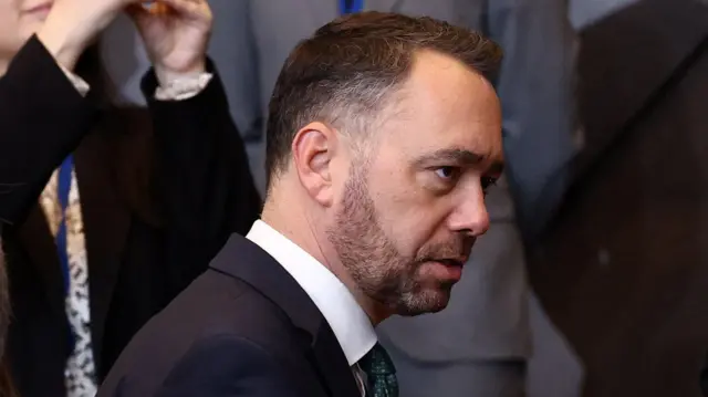 ماکسیم پرِوو، وزیر خارجه بلژیک، کت تیره و کراوات سبز تیره بر تن دارد و افرادی در پسزمینه دیده میشوند.