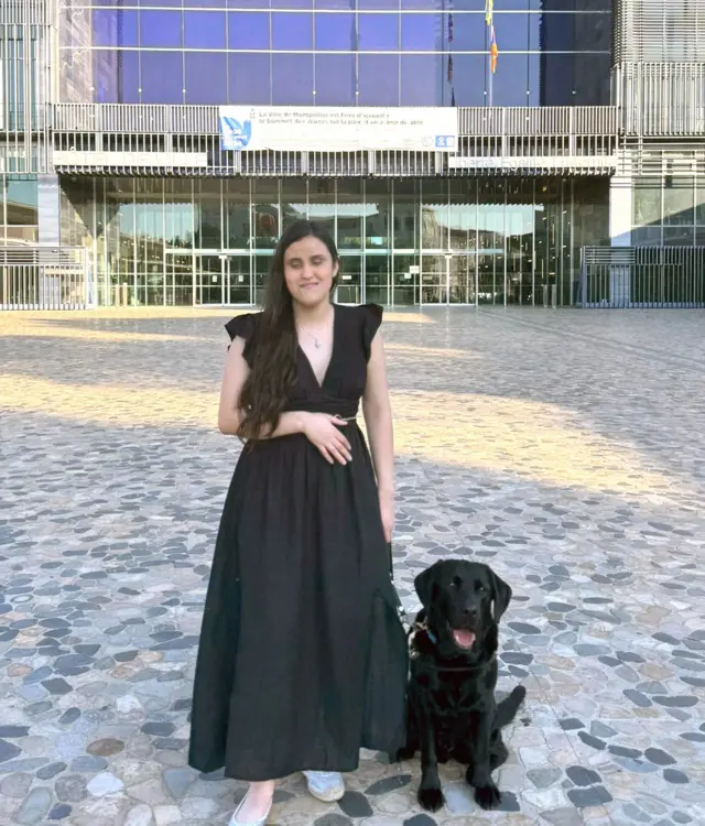 视障人士站在BBC总部大楼前,她牵着一只黑色拉布拉多猎犬