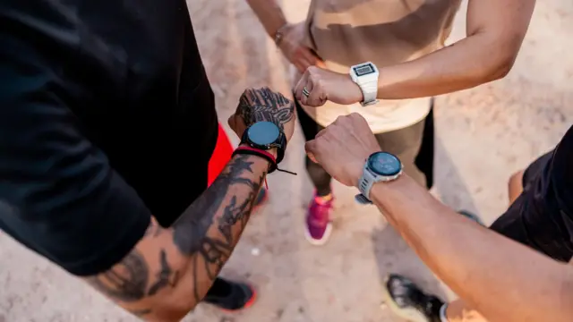 三名跑者低头查看手腕上的智能手表,照片从上方拍摄,焦点集中在他们的手臂与手腕