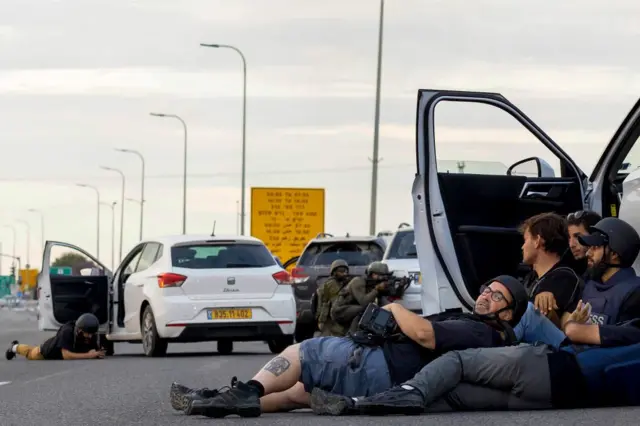 صحفيون يحتمون خلف السيارات بينما يتخذ جنود إسرائيليون مواقعهم خلال اشتباكات مع مقاتلين فلسطينيين، في 7 أكتوبر 2023.