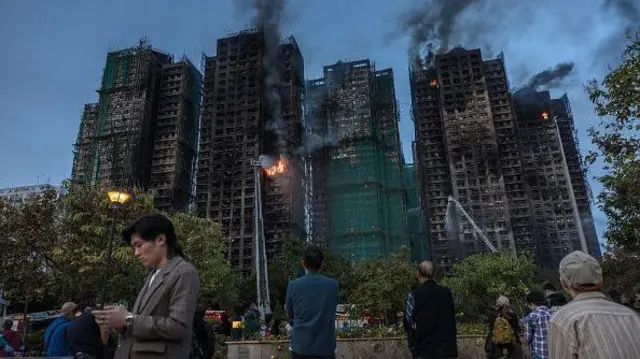 2025年11月26日,香港大埔区宏福苑住宅大楼发生大火,浓烟从公寓大楼内升起。屋苑外有多名巿民站着,或看着火势,或盯着电话屏幕。