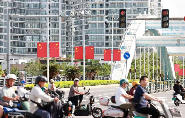 طريق في مقاطعة في الصين مزين بالأعلام الصينية ويمر عبره راكبو درجات نارية