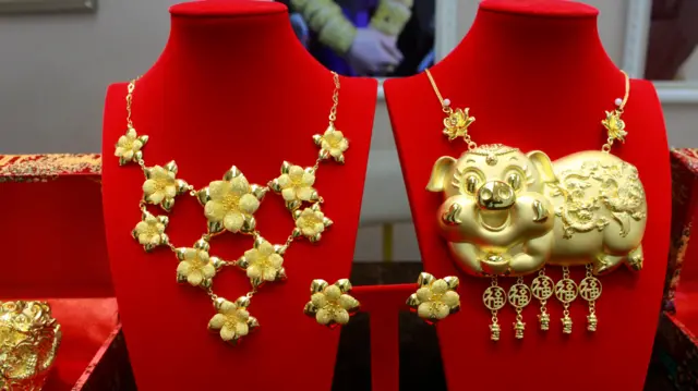 两款金器的近照,左边是花形图案的金项链,右边是金猪牌。