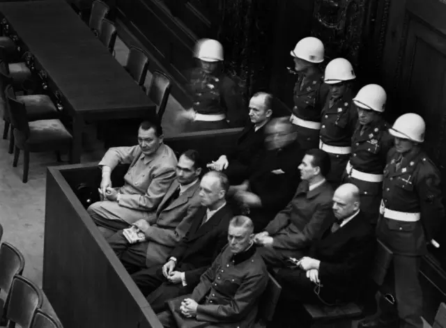 हर्मन गोरिंग (नाझी हवाई दलाचा माजी प्रमुख), रुडॉल्फ हेस (माजी डेप्युटी चान्सलर), जोआकिम वॉन रिबेनट्रॉप (माजी परराष्ट्र मंत्री), आणि विल्हेल्म कीटेल (माजी नाझी लष्करप्रमुख) यांचा फोटो, ते ��्युरेंबर्ग पॅलेस ऑफ जस्टिसच्या कोर्टरूममध्ये बसलेले होते