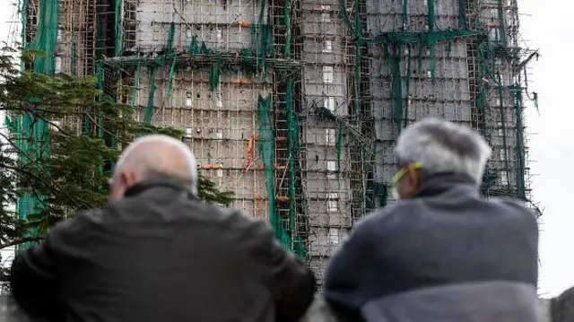 香港大埔区宏福苑住宅大楼发生火灾,损毁严重。两名头有白发的男子看着楼宇。