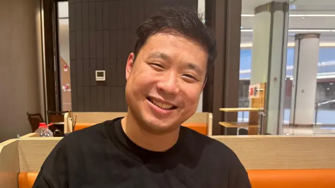 25岁的孙展在南京的火锅餐厅当服务员,对着镜头微笑并侧头拍照,这张照片看起来像是餐厅里的场景