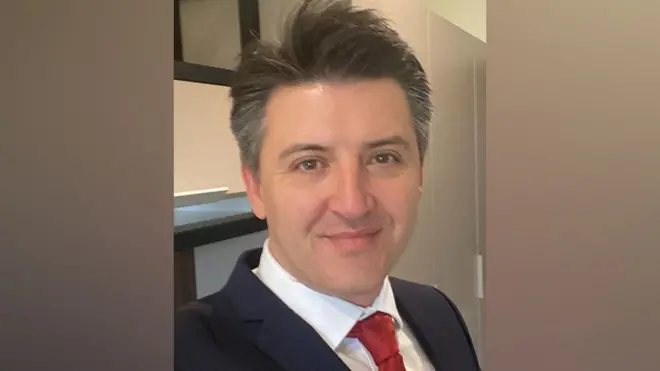 佐尼身穿深色西装,并且微笑望向镜头。