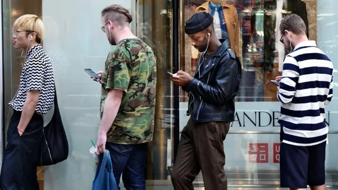 四个男人排成一队,看着自己的智慧型手机。