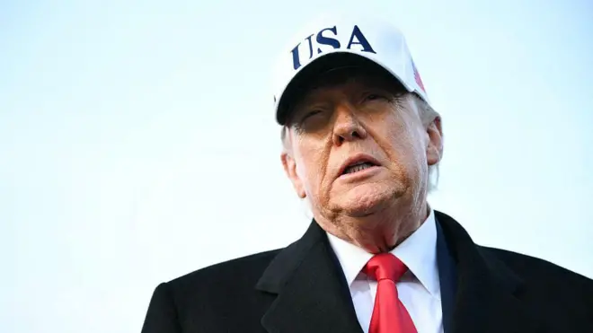 US President Donald Trump speaks to journalists upon returning to Joint Base Andrews in Maryland. He is wearing a white hat with the words USA on it.