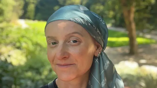 لوئیزا توسکانو در حین درمان، شال سبزی را روی سر بسته است. او با آرامش به دوربین نگاه میکند