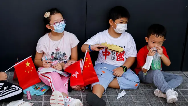 中共建政周年“十一国庆”香港一群小孩手持中国国旗与香港特区区旗坐在路旁休息(资料图片)