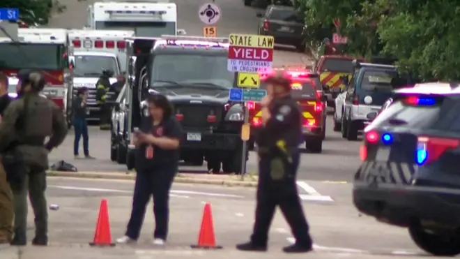 موقع الحدث حيث تقف عناصر أمنية وسيارات شرطة في الصورة الملتقطة نهاراً.