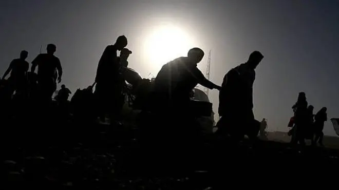 تصویر شماری از مهاجرانی که ازپاکستان به افغانستان اخراج شده اند. تصویر تاریک است چهرههای شان معلوم نمیشود اما مهاجران در یک قطار همه به سمت راست تصویر درحرکت هستند.