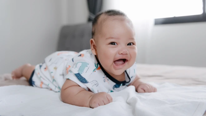 A smiling baby boy lying on his tummy on a bed
ඇඳක් මත වැතිර සිටින පිරිමි ළමයෙක්
