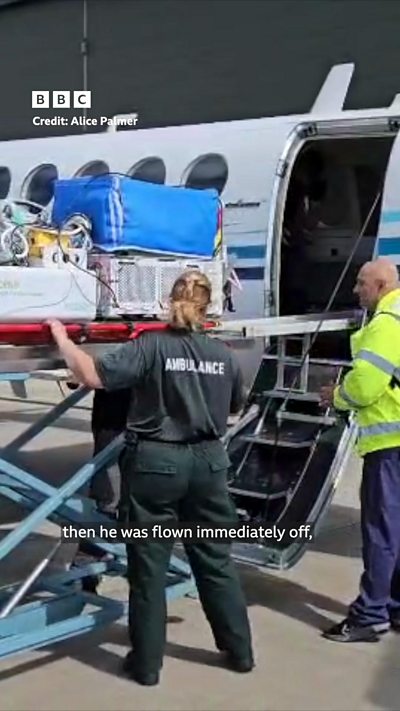 A specialist incubator is wheeled onto a medical jet by an ambulance worker