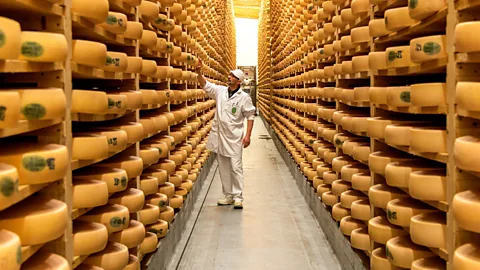 Man in white clothes standing between shelves stacked with yellow Comte wheels inside Le Fort Saint-Antoine in the Jura, France (Credit: Alain Doire/BFC Tourisme)