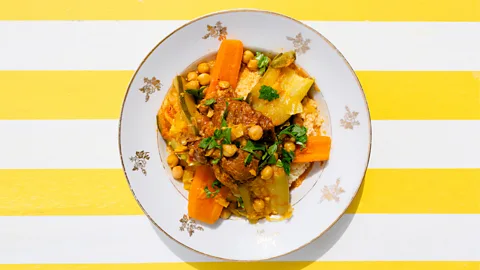 Plate of stew with chickpeas and couscous on yellow and white striped background (Credit: Caroline Dutrey)